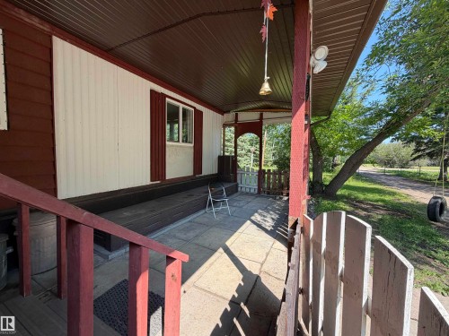 Covered front porch featuring a brown metal roof, red painted wood railings, and a concrete patio - # 501  11131 Twp Rd 600, Rural St. Paul County, AB - Outdoor With Exterior