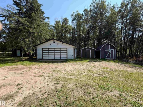 White garage with a paneled garage door and dark trim, accompanied by two storage sheds - # 501  11131 Twp Rd 600, Rural St. Paul County, AB - Outdoor