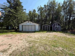 White garage with a paneled garage door and dark trim, accompanied by two storage sheds - 
