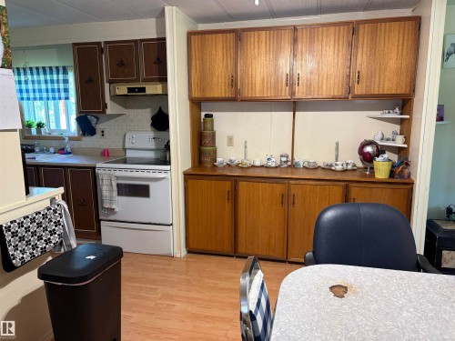 Kitchen space featuring wood-finish flooring, two-tone cabinetry with dark brown and lighter wood finishes, and a window with a valance - # 501  11131 Twp Rd 600, Rural St. Paul County, AB - Indoor Photo Showing Kitchen