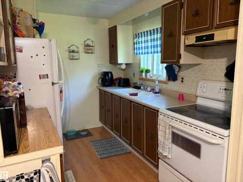 Kitchen featuring wood-finish flooring, white appliances, dark wood-finish cabinetry, and a window above the sink - # 501  11131 Twp Rd 600, Rural St. Paul County, AB - Indoor Photo Showing Kitchen