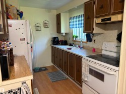 Kitchen featuring wood-finish flooring, white appliances, dark wood-finish cabinetry, and a window above the sink - 