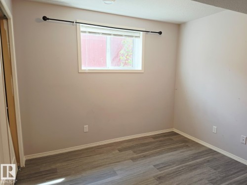 Room featuring wood-finish flooring, neutral wall tones, white baseboards, and a window with white trim - 123 Rue Masson, Beaumont, AB - Indoor Photo Showing Other Room