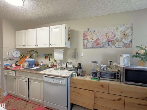 Kitchen featuring white upper and lower cabinetry, a stainless steel dishwasher, and light-toned countertops - #108 4501 51 St, Leduc, AB - Indoor Photo Showing Kitchen