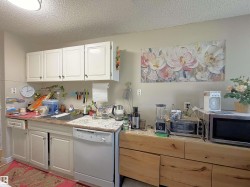 Kitchen featuring white upper and lower cabinetry, a stainless steel dishwasher, and light-toned countertops - 
