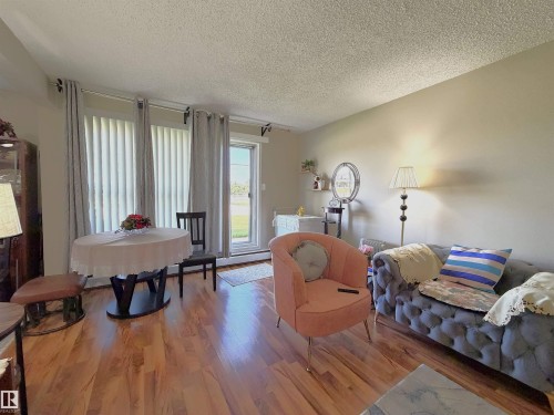 Living area featuring wood-finish flooring, light-toned walls, and a sliding glass door with vertical blinds and drapery rods - #108 4501 51 St, Leduc, AB - Indoor Photo Showing Living Room