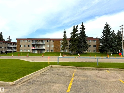 Multi-unit building featuring a brick and stucco facade, private balconies, and mature evergreen landscaping - #108 4501 51 St, Leduc, AB - Outdoor