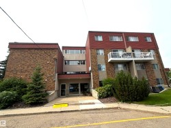 Multi-story building featuring a brick and stucco exterior, red shingle roofing, and multiple balconies with white railings - 