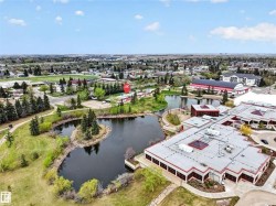 Aerial perspective featuring a building with a flat roof and red trim, surrounded by a landscaped pond with a small island - 