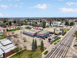 Commercial building featuring a dark facade with a pink accent stripe, expansive paved parking lot, street frontage, and mature evergreen trees - 
