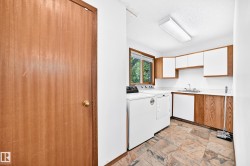 Functional laundry area featuring stone-finish flooring, a window offering natural light, white upper cabinetry, and wood-finish lower cabinetry with a built-in sink - 