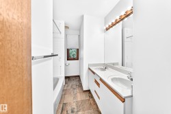 Bathroom featuring a dual vanity with integrated sinks, a wood-trimmed mirror, and a white bathtub with tile surround - 