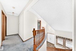 Curved wooden banister overlooking a lower level, featuring a light blue carpeted hallway with wood-finish doors, and a skylight - 