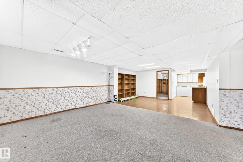 Spacious finished basement featuring a drop ceiling with integrated lighting, built-in shelving, and a partial kitchen area with white cabinetry and a wood-finish countertop - 4208 Ramsay Road Nw, Edmonton, AB - Indoor Photo Showing Other Room