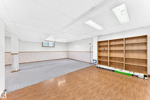 Spacious room featuring wood-finish flooring, light grey carpeting, built-in shelving, and a drop ceiling with recessed lighting - 4208 Ramsay Road Nw, Edmonton, AB - Indoor Photo Showing Other Room