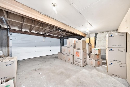 Concrete floor garage with a white sectional door, exposed ceiling joists, and a bare bulb light fixture - 4208 Ramsay Road Nw, Edmonton, AB - Indoor Photo Showing Garage