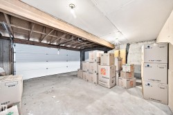 Concrete floor garage with a white sectional door, exposed ceiling joists, and a bare bulb light fixture - 
