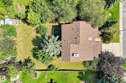 Residential property featuring a brown shingle roof, mature trees, a green lawn, and a paved driveway - 