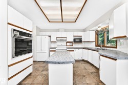 Kitchen featuring white cabinetry with wood-tone accents, a built-in wall oven, a center island with a gray countertop, and tile flooring - 