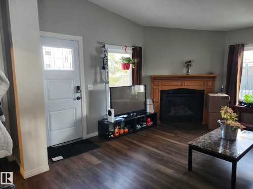 Living area featuring wood-finish flooring and a fireplace with a wood mantle and black insert - 5273 50 Street, Mayerthorpe, AB - Indoor Photo Showing Living Room With Fireplace