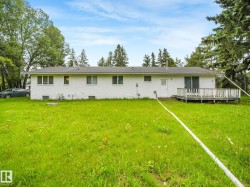 Expansive green space featuring a white brick exterior, multiple windows, a rear entry door, a sliding glass door, and a wooden deck - 