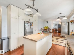 Kitchen featuring an integrated refrigerator, white cabinetry with dark hardware, a center island with a light-toned countertop, wood-finish flooring, and pendant lighting - 