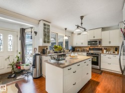 Kitchen featuring white cabinetry, wood-finish flooring, a central island with countertop, stainless steel appliances, and a tiled backsplash - 