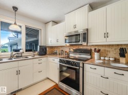 Kitchen featuring white beadboard cabinetry, stainless steel appliances, a tile backsplash, and a double basin sink - 