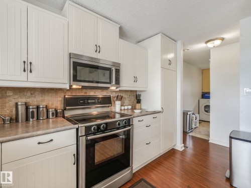 Kitchen featuring white cabinetry, stainless steel appliances, tile backsplash, and wood-finish flooring - 10912 5 Avenue Sw, Edmonton, AB - Indoor Photo Showing Kitchen