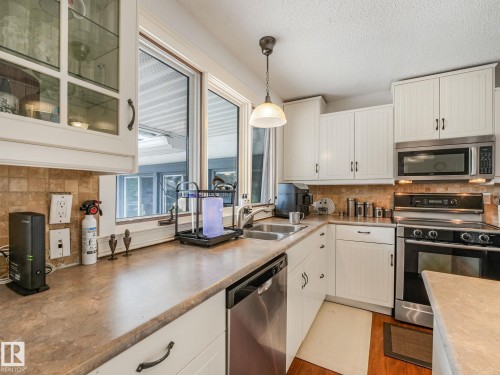 Kitchen featuring white cabinetry, stainless steel appliances, a double basin sink, and wood-finish flooring - 10912 5 Avenue Sw, Edmonton, AB - Indoor Photo Showing Kitchen With Double Sink