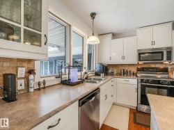 Kitchen featuring white cabinetry, stainless steel appliances, a double basin sink, and wood-finish flooring - 