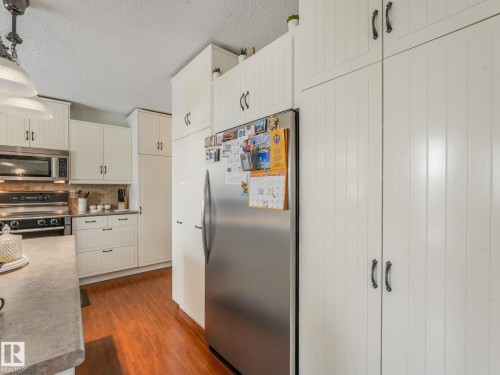 Kitchen featuring extensive white cabinetry with black hardware, wood-finish flooring, a stainless steel refrigerator, and a built-in microwave above a range - 10912 5 Avenue Sw, Edmonton, AB - Indoor Photo Showing Kitchen