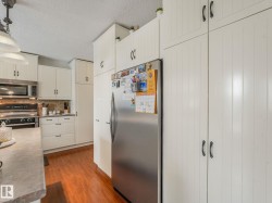 Kitchen featuring extensive white cabinetry with black hardware, wood-finish flooring, a stainless steel refrigerator, and a built-in microwave above a range - 