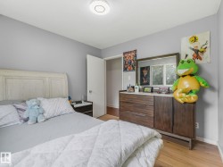 Bedroom featuring light gray walls, wood-finish flooring, a contemporary ceiling light fixture, and a window with natural light - 