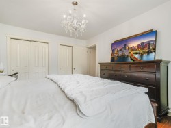 Bright bedroom featuring a crystal chandelier, wood-finish flooring, white walls, and bi-fold closet doors - 