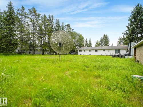 Expansive green space featuring a large lawn area, mature evergreen trees, and a white one-story residence with a sliding glass door - 10912 5 Avenue Sw, Edmonton, AB - Outdoor