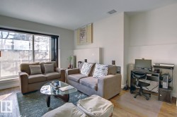 Spacious living area featuring large windows, wood-finish flooring, and light neutral wall tones - 