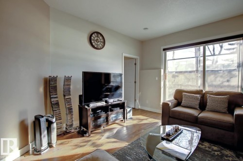 Living area with wood-finish flooring, light-toned walls, and a large window - 102 10905 109 Street, Edmonton, AB - Indoor Photo Showing Living Room
