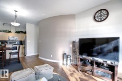 Open-concept living space featuring wood-finish flooring, a contemporary curved accent wall, and a kitchen with light wood cabinetry and stainless steel appliances - 