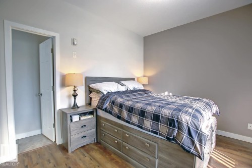 Bedroom featuring wood-finish flooring, light grey walls, and a darker accent wall - 102 10905 109 Street, Edmonton, AB - Indoor Photo Showing Bedroom