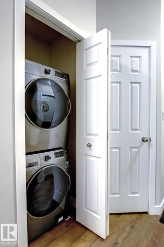 Dedicated laundry closet featuring a stackable washer and dryer, wood-finish flooring, white paneled doors, and brushed nickel hardware - 102 10905 109 Street, Edmonton, AB - Indoor Photo Showing Laundry Room