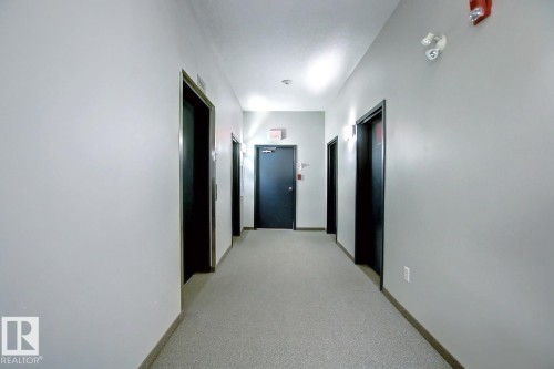 Hallway with light gray walls, dark gray doors, and light gray carpeted flooring - 102 10905 109 Street, Edmonton, AB - Indoor Photo Showing Other Room