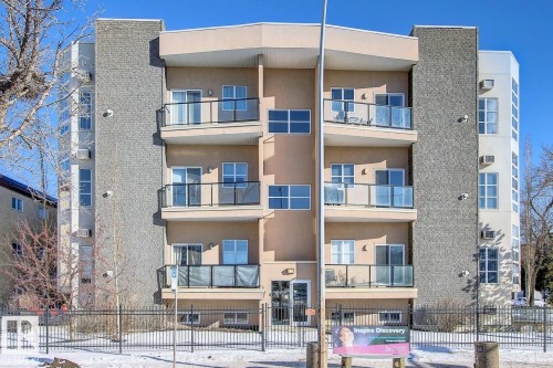 Multi-story building featuring a stucco and stone facade, private balconies with glass railings, large windows, and a secure perimeter fence - 102 10905 109 Street, Edmonton, AB - Outdoor