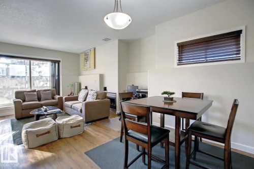 Open-concept living area featuring wood-finish flooring, a built-in fireplace, and a large sliding glass door - 102 10905 109 Street, Edmonton, AB - Indoor