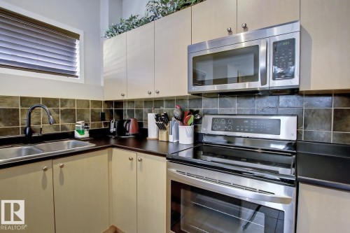 Corner kitchen with stainless steel appliances, dual basin sink, black countertop, and tile backsplash - 102 10905 109 Street, Edmonton, AB - Indoor Photo Showing Kitchen With Double Sink