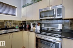 Corner kitchen with stainless steel appliances, dual basin sink, black countertop, and tile backsplash - 