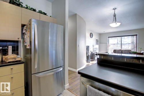 Stainless steel French door refrigerator set within light wood-finish cabinetry, featuring a dark tile backsplash and dark countertops - 102 10905 109 Street, Edmonton, AB - Indoor Photo Showing Kitchen