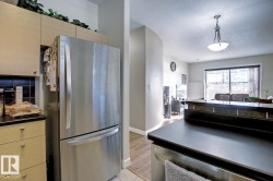 Stainless steel French door refrigerator set within light wood-finish cabinetry, featuring a dark tile backsplash and dark countertops - 