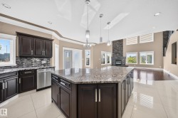 Spacious kitchen and living area featuring a large central island with a granite countertop, dark wood cabinetry, stainless steel appliances, and tile flooring - 