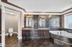 Spacious bathroom featuring dark wood cabinetry, granite countertops, dual sinks, a large corner soaking tub, and a separate water closet - 